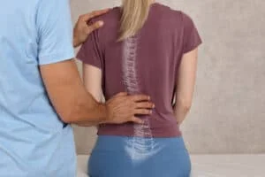 Chiropractor examining a patient's back for scoliosis or spinal misalignment with hands on the spine.