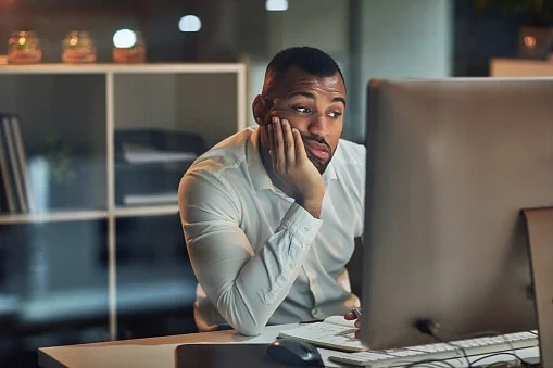 Man looking frustrated at his computer screen, possibly experiencing stress or difficulty with work or health issues.