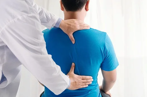 Chiropractor performing spinal assessment on patient with back pain in clinic setting.