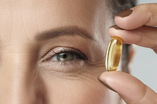 Close-up of a woman holding a fish oil capsule near her eye, emphasizing health benefits for spinal and overall wellness.