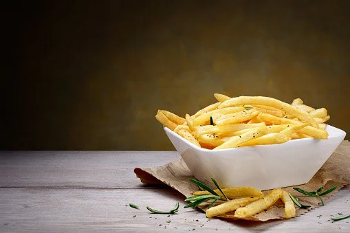 A bowl of crispy French fries on a wooden table with a dark background, suitable for food and restaurant SEO.
