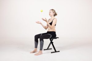 ScoliBalance Scoliosis Exercises 8 Young girl sitting on a bench, playing with a tennis ball, demonstrating spinal health and posture, related to scoliosis and chiropractic care in Louisiana.