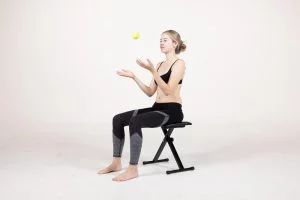 Young girl sitting on a bench, playing with a tennis ball, demonstrating spinal health and posture, related to scoliosis and chiropractic care in Louisiana.