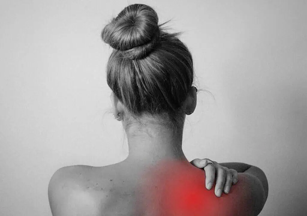 Back view of woman experiencing shoulder pain, holding her shoulder with her hand, highlighting discomfort area.